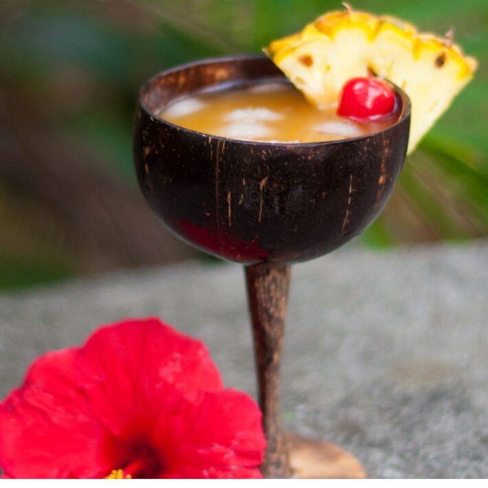 Lili Coco Tini Recipe with a pineapple wedge and cherry on the rim of a wood martini long stem cup