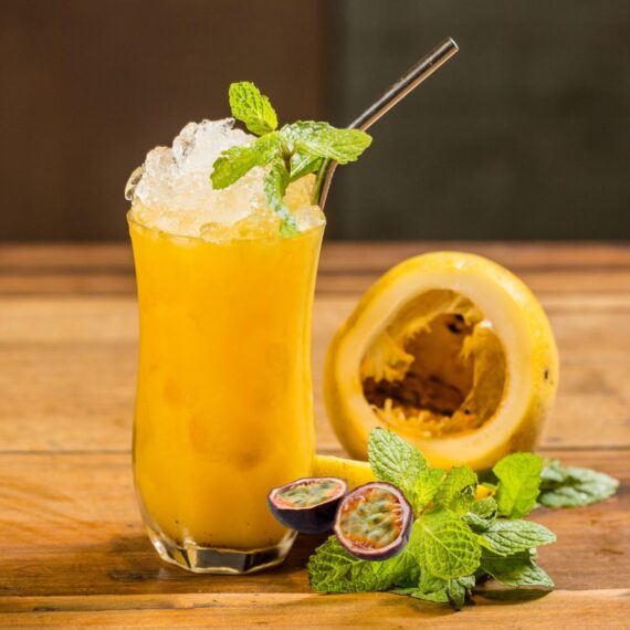 Passion Fruit Fizz Mocktail Recipe in a tall glass with a sprig of mint and a passion fruit rind on the table