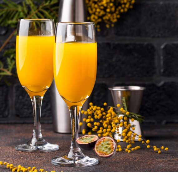 2 Passion Fruit Mimosa Recipe in champagne flutes with a sprig of small yellow flowers and passion fruit on the table