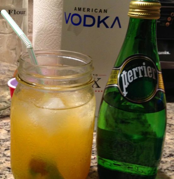 Tall Nani Recipe with in a glass with a lime and a straw along side a bottle of perrier