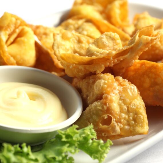 Brie Filled Won Tons on a white platter with a passion fruit dipping sauce in a white ramekin