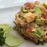 Passion Fruit Ceviche With Avocado with a twisted lime slice on a white plate