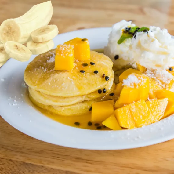 Banana Pancake With Passion Fruit Syrup and Mangoes on a white plate