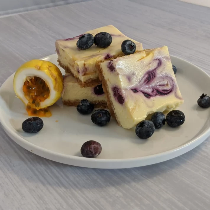 Passion Fruit Blueberry Swirl Cheesecake Bars garnished with blueberries and an open passion fruit