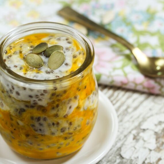 A small glass jar with a tropical passion fruit chia pudding in it garnished with pumpkin seeds