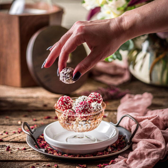 A female hand taking a Passion Fruit Milk Chocolate Hand Rolled Truffle out of a bowl of red and white truffles